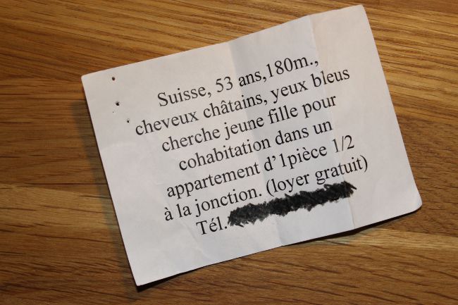 Paper with text: Suisse, 53 ans, 180m, cheveux châtains, yeux bleus cherche jeune fille pour cohabitation dans un appartement d' 1 piece ½ a la joncyion (loyer gratuit).